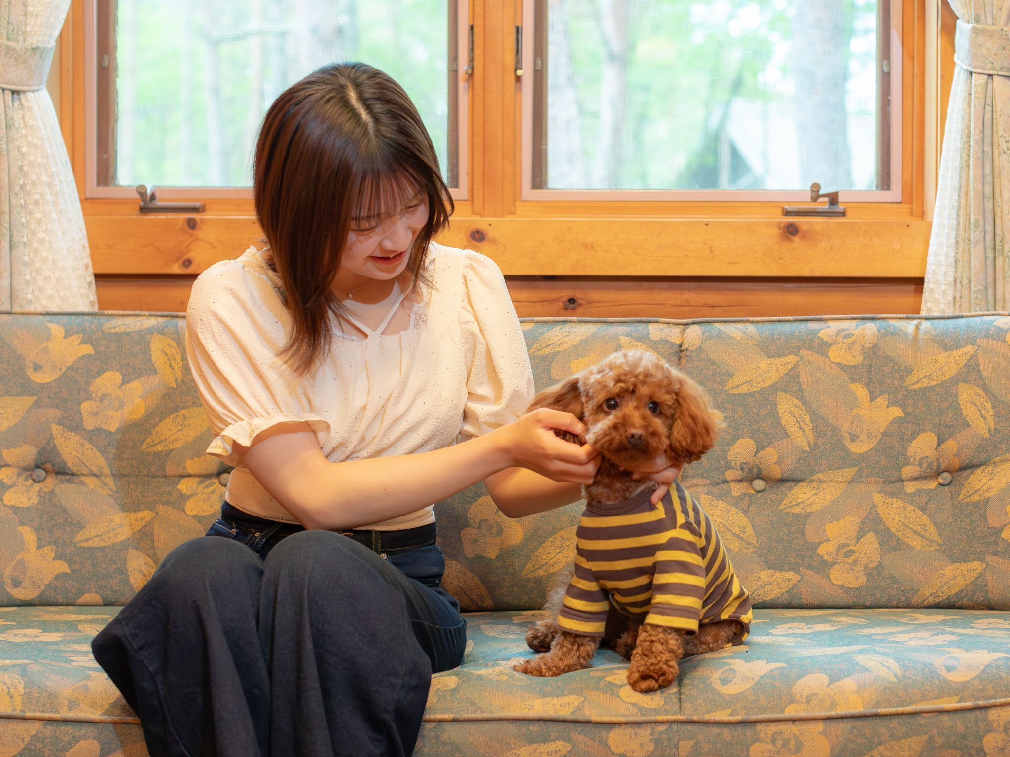 A person sitting on a patterned sofa with a dog wearing a striped outfit.
