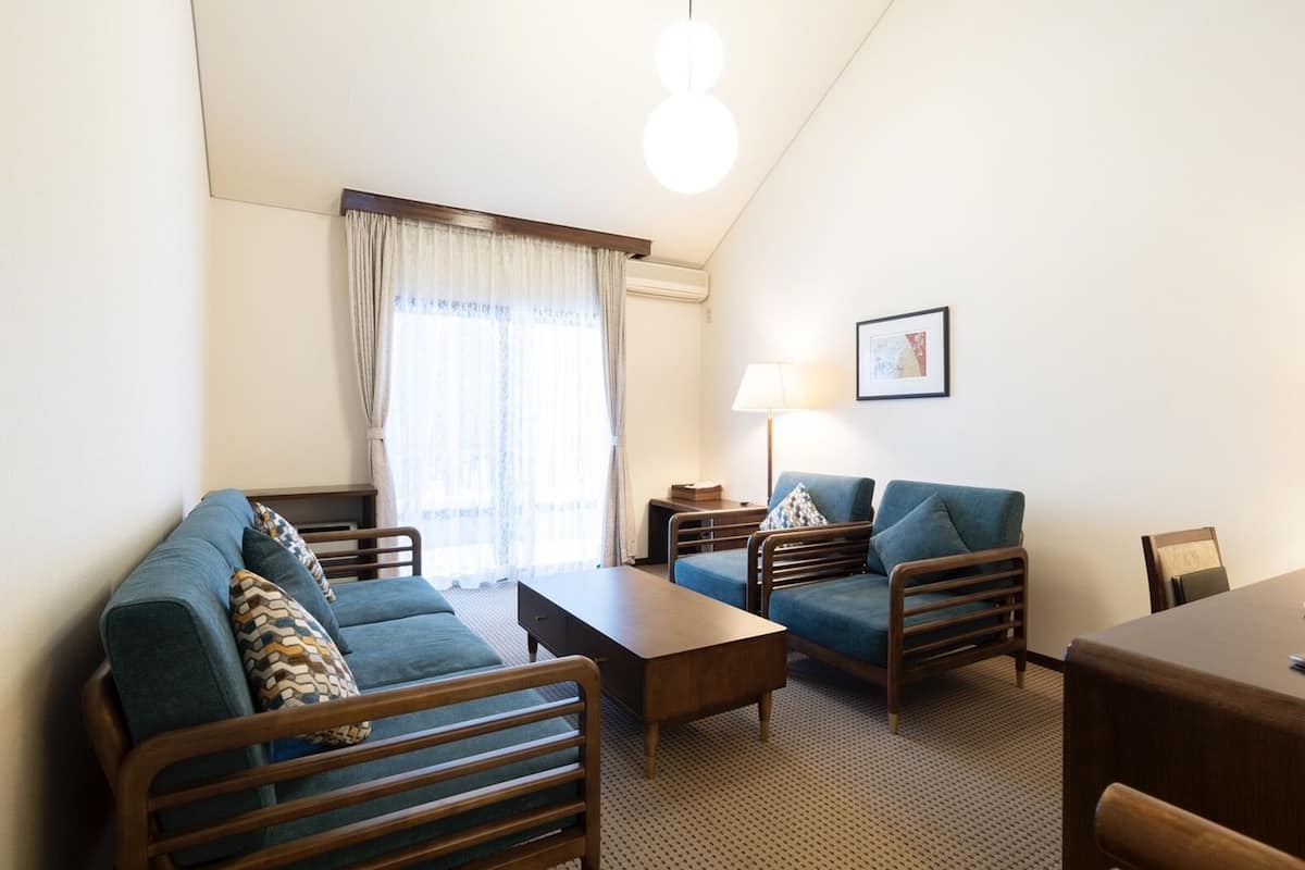 Una sala de estar compacta con un sofá, sillones, una mesa de centro y una lámpara.
