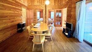 A wooden cabin interior with a dining table, chairs, a television, and a bed in the background. - Holiday Villa Hotel & Resort Karuizawa (Tsumagoi)