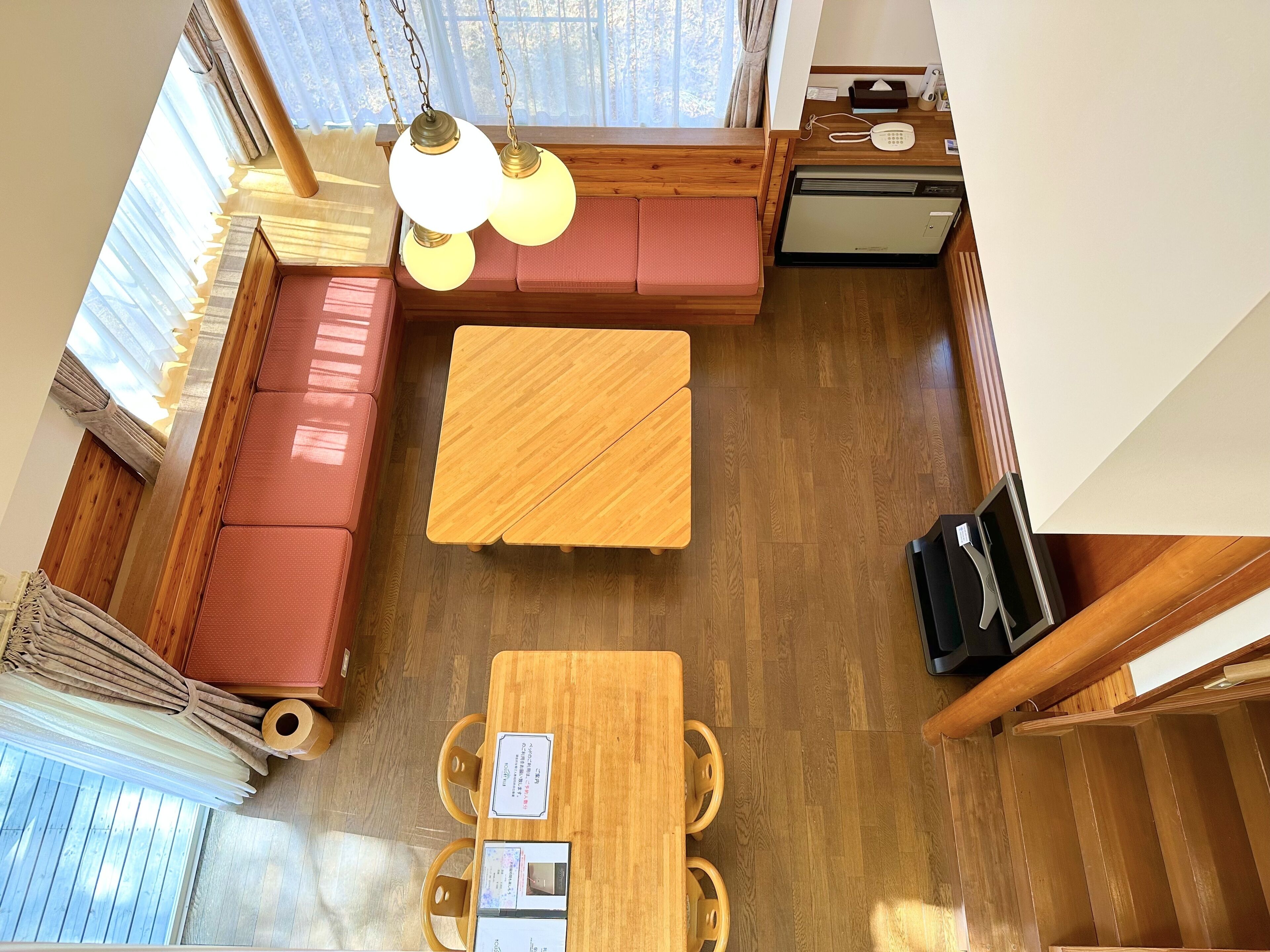 A room with a wooden floor, a red sofa, a wooden table, and a ceiling fan.