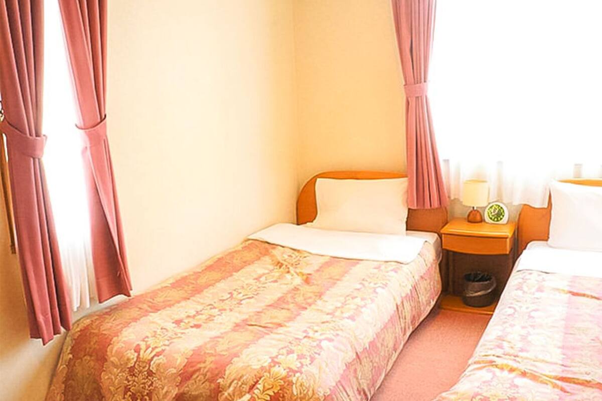 A hotel room with two single beds, a nightstand with a lamp, and a window with curtains.
