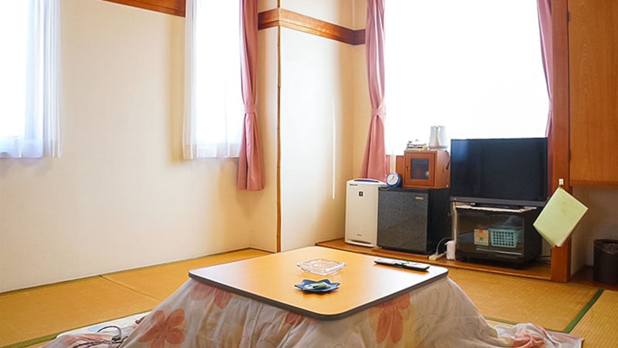 Ein Zimmer mit Tatami-Boden, einem niedrigen Tisch mit Fernbedienung, einem Fernseher, einer Mikrowelle und einem kleinen Schrank.