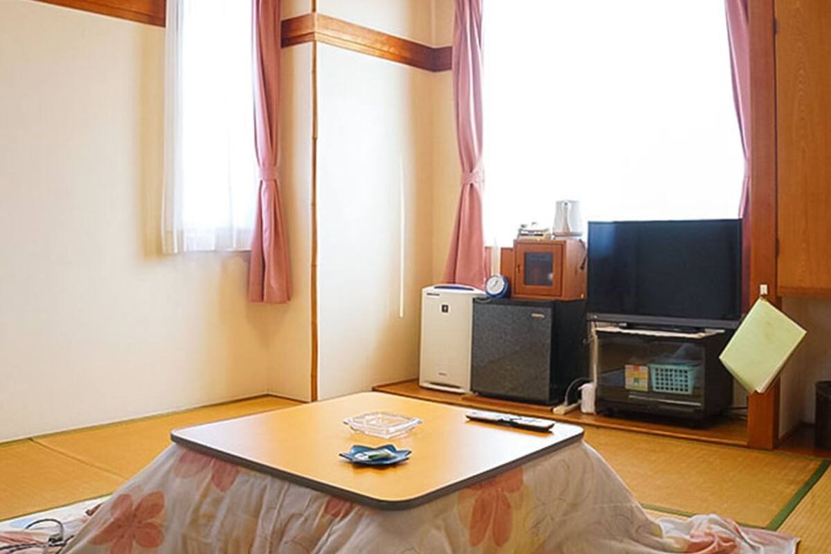 A room with tatami flooring, a low table with a remote control, a television, a small refrigerator, and a microwave.