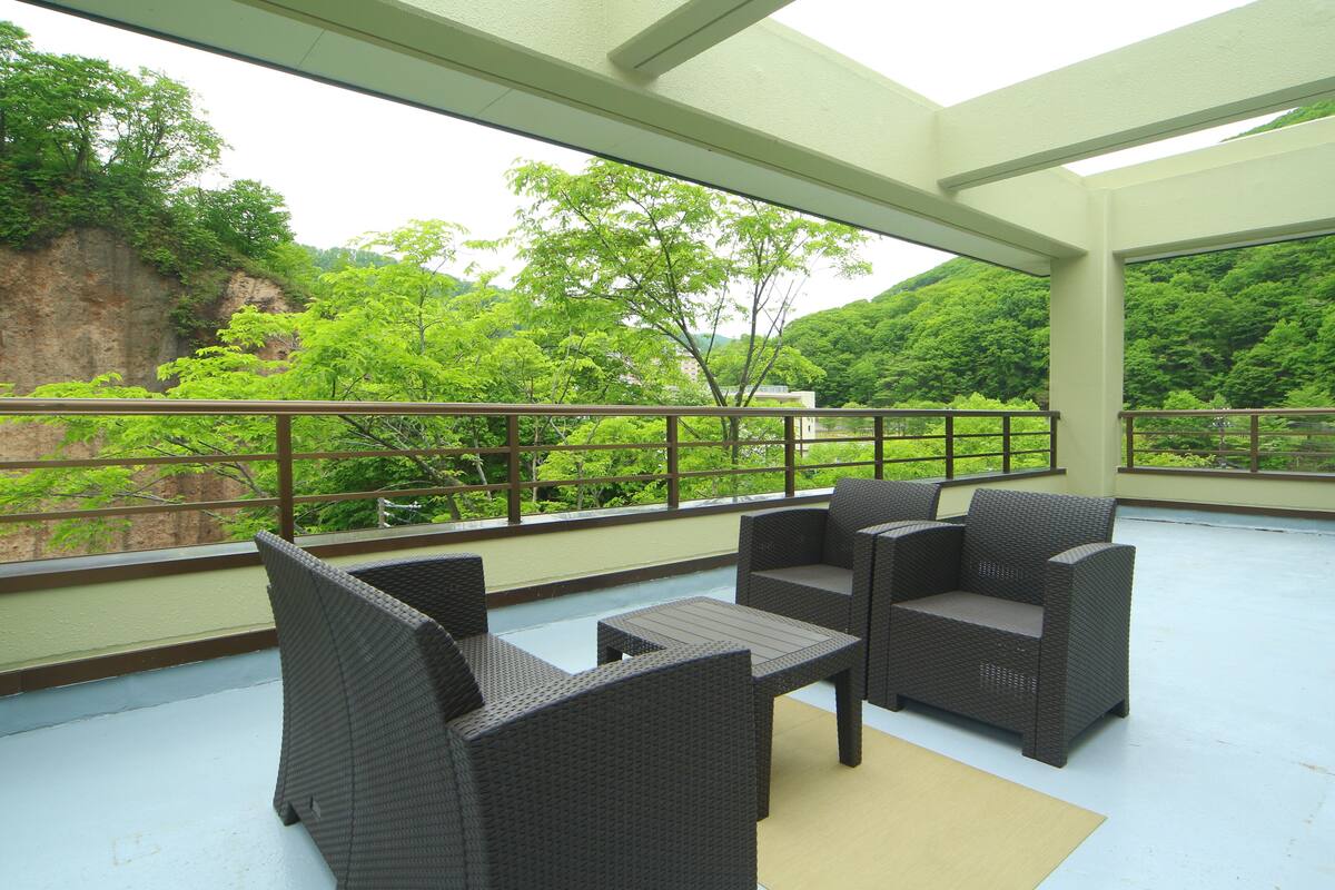 A covered outdoor seating area with wicker furniture and a view of lush greenery and a cliff.