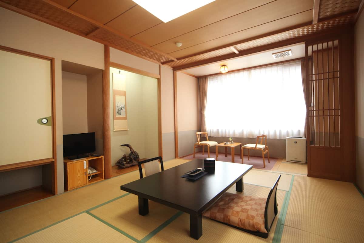 A traditional Japanese room with tatami flooring, a low table, chairs, a television, and sliding doors.