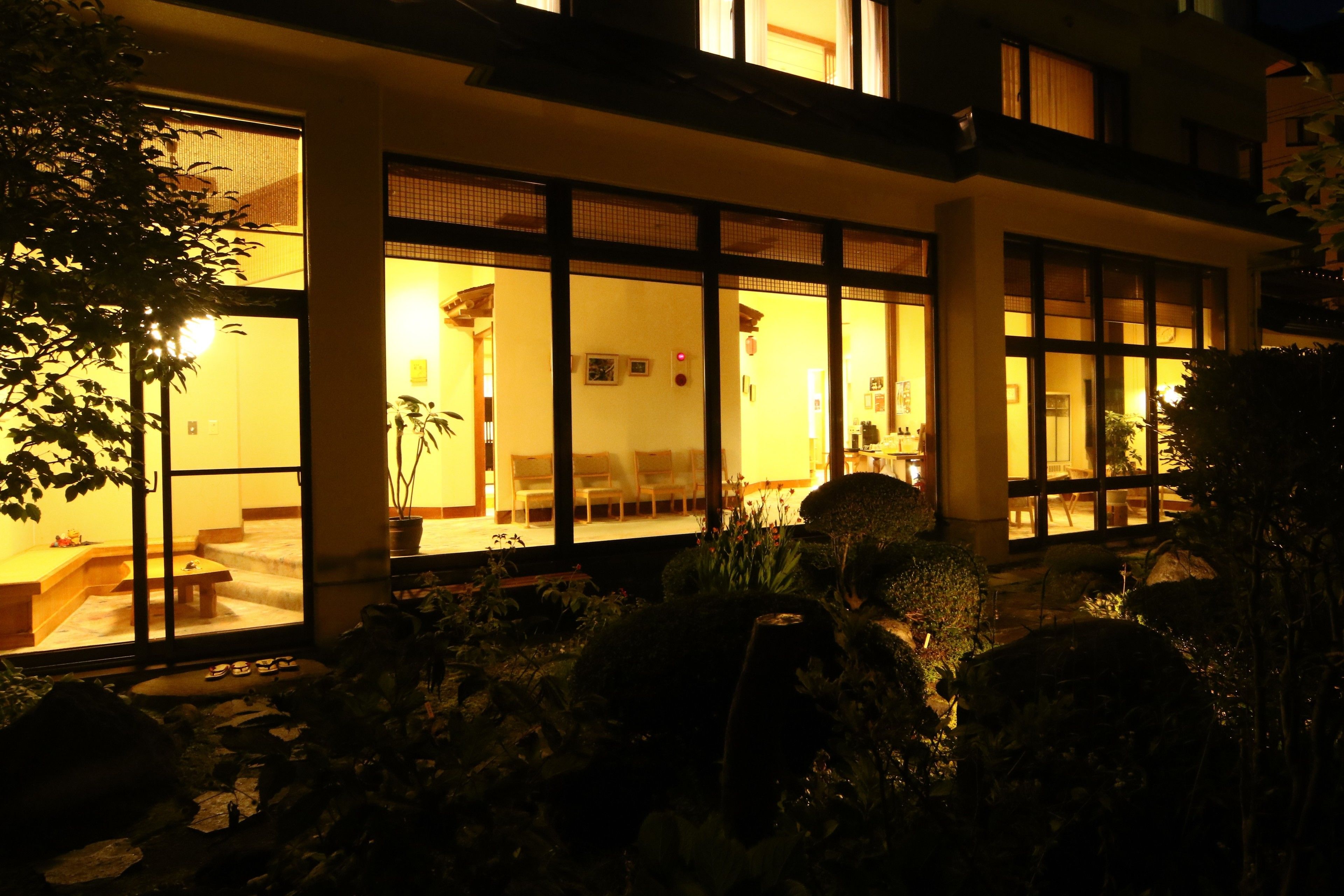 A modern building with large glass windows, a stone pathway, and a well-maintained garden.