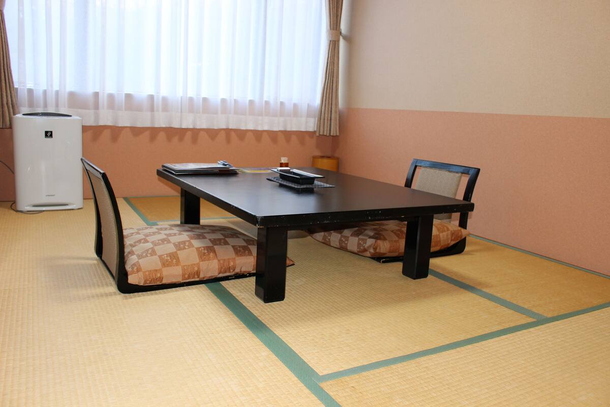 A room with tatami flooring, a table with chairs, and a heater.