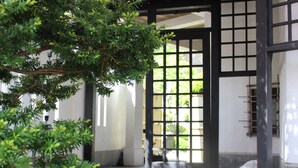 Un torii japonés tradicional con estructura de madera y diseño de cuadrícula, que da acceso a un edificio de paredes blancas y piso de baldosas.