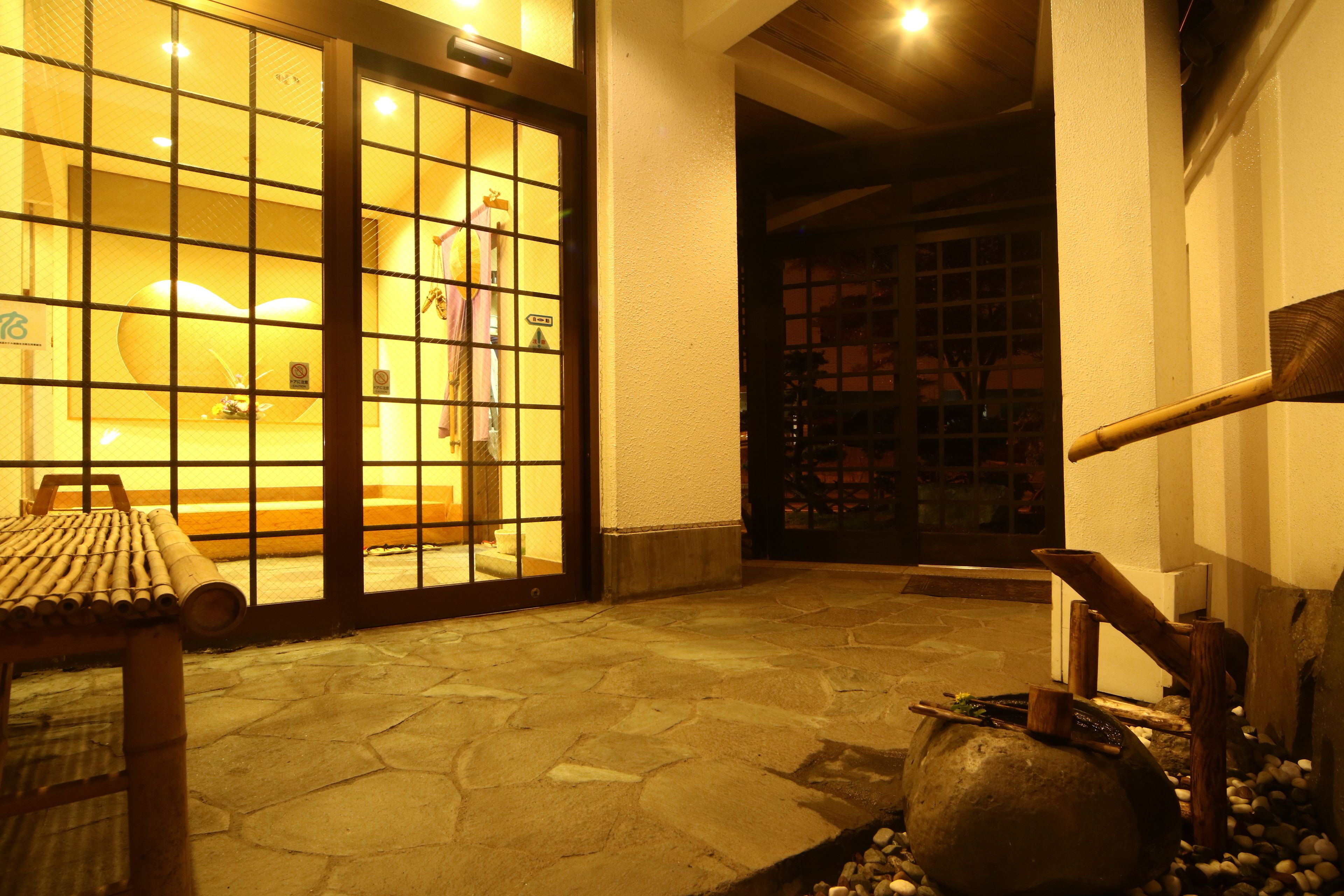 A traditional Japanese entrance with a tiled floor, a wooden bench, and a stone lantern.