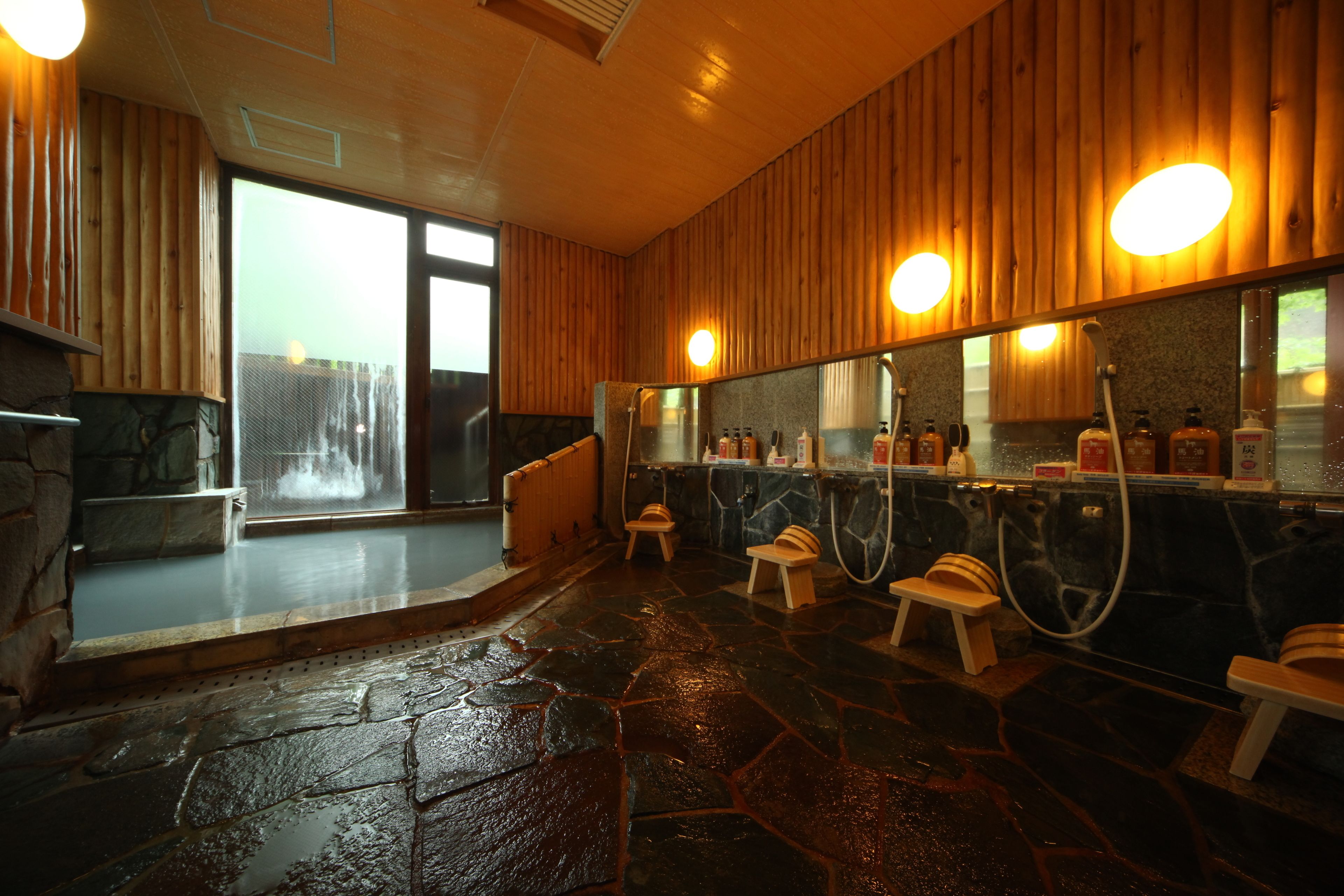 A stone-floored bathroom with wooden walls, a large mirror, and a bench.