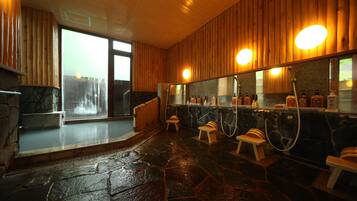 A stone-floored bathroom with wooden walls, a large mirror, and a bench.