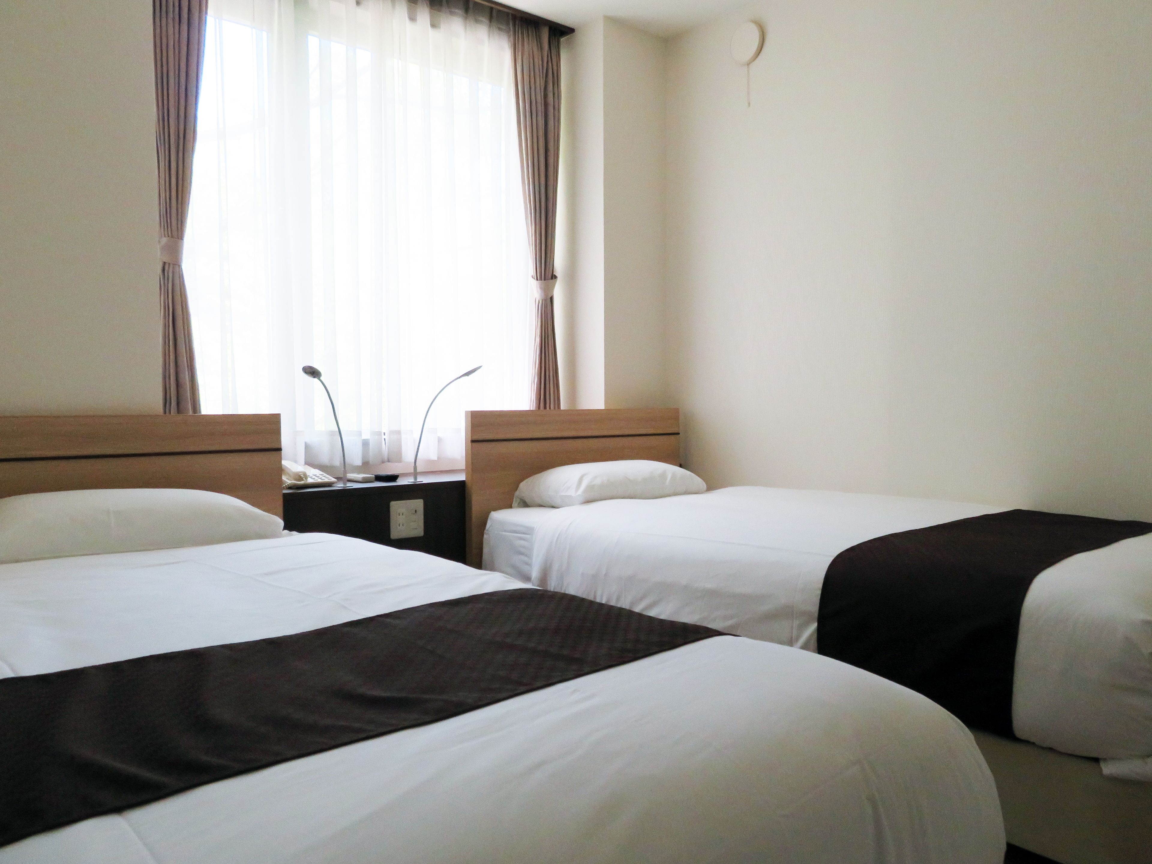Une chambre d’hôtel avec deux lits simples, une table de chevet avec une lampe et une fenêtre avec des rideaux.