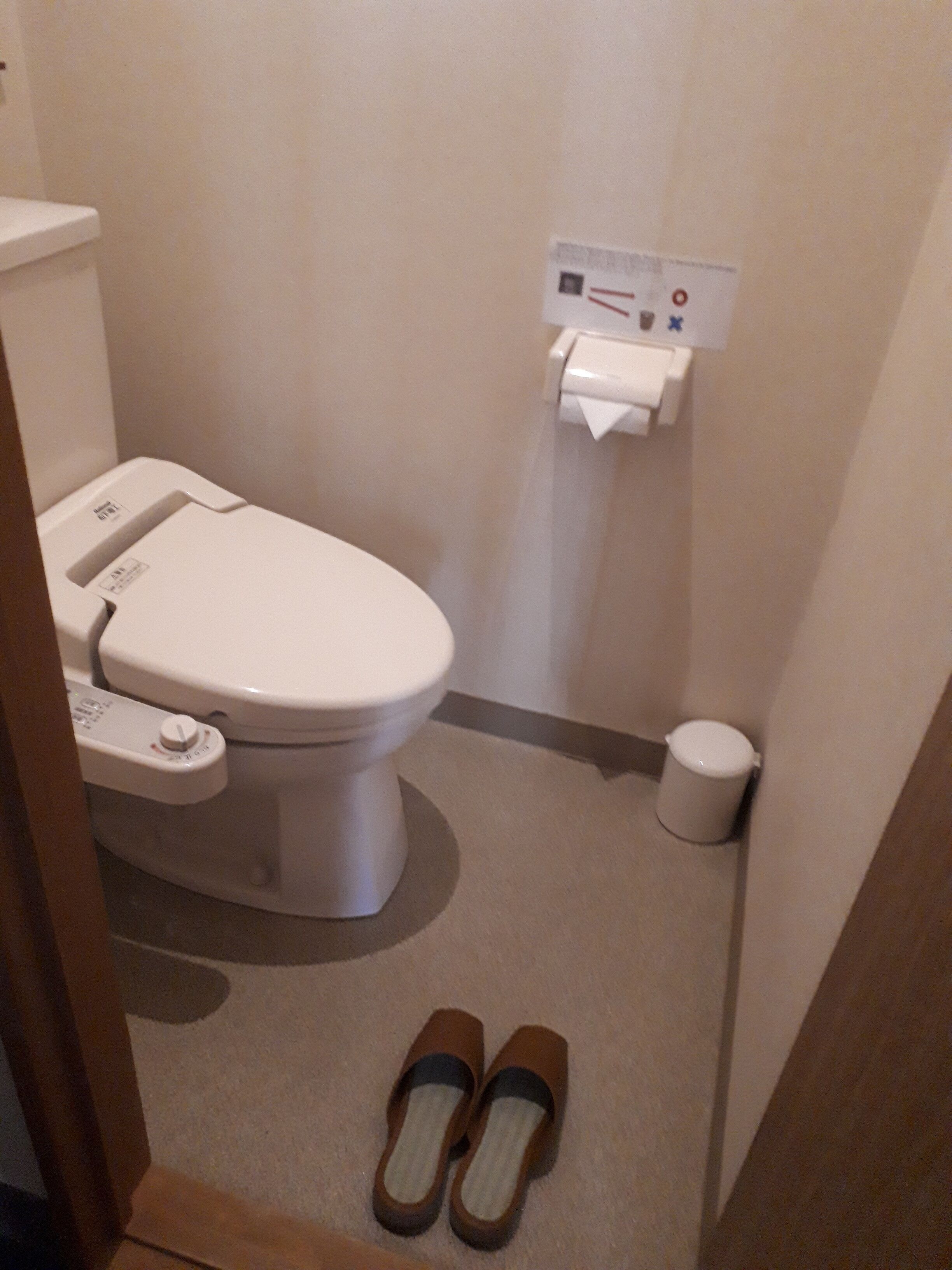 Un baño pequeño con inodoro, dispensador de toallas de papel y un cubo de basura.