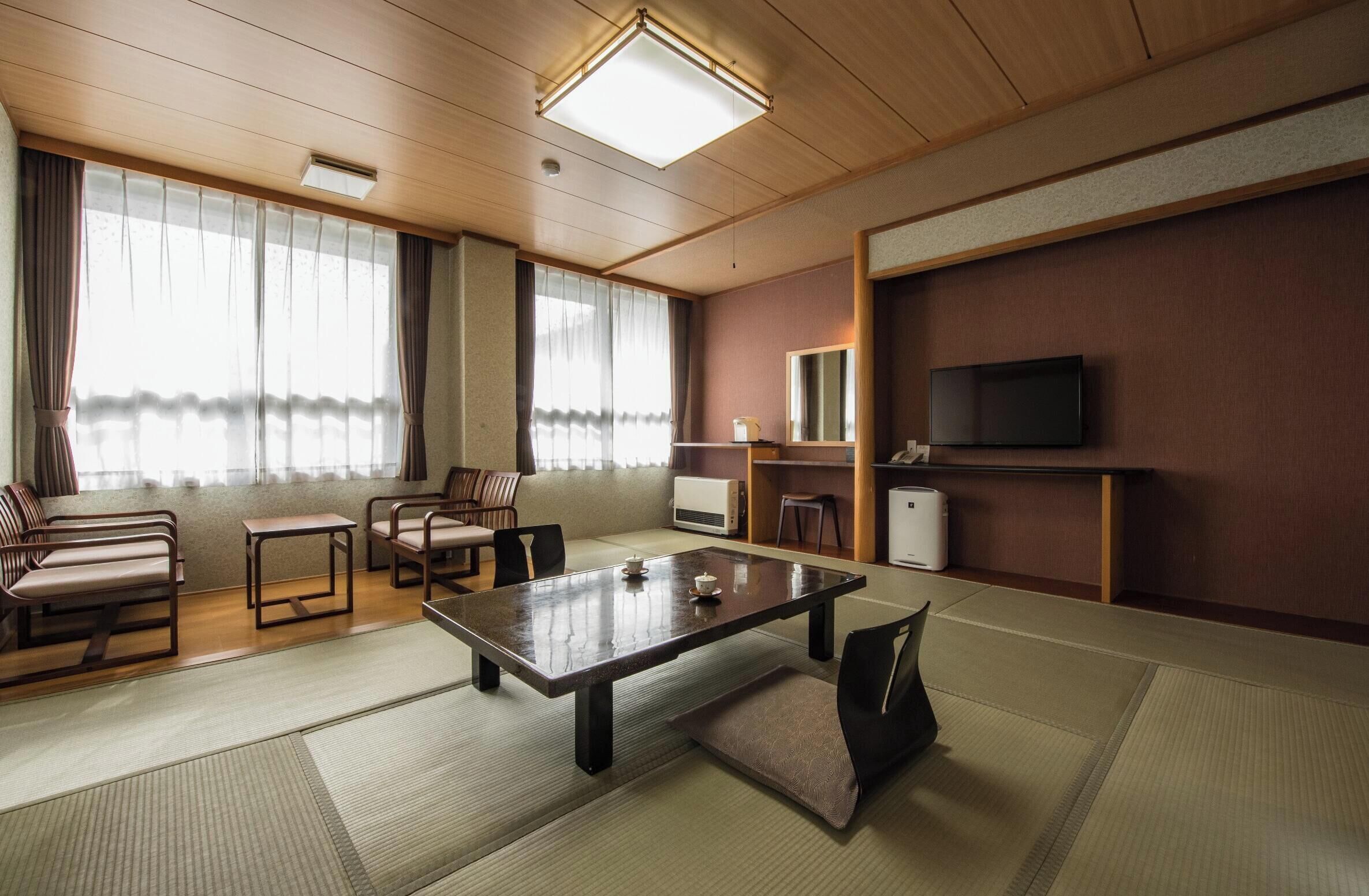 A room with tatami mats, a low table with a tea set, wooden furniture, a television, and a large window with curtains.