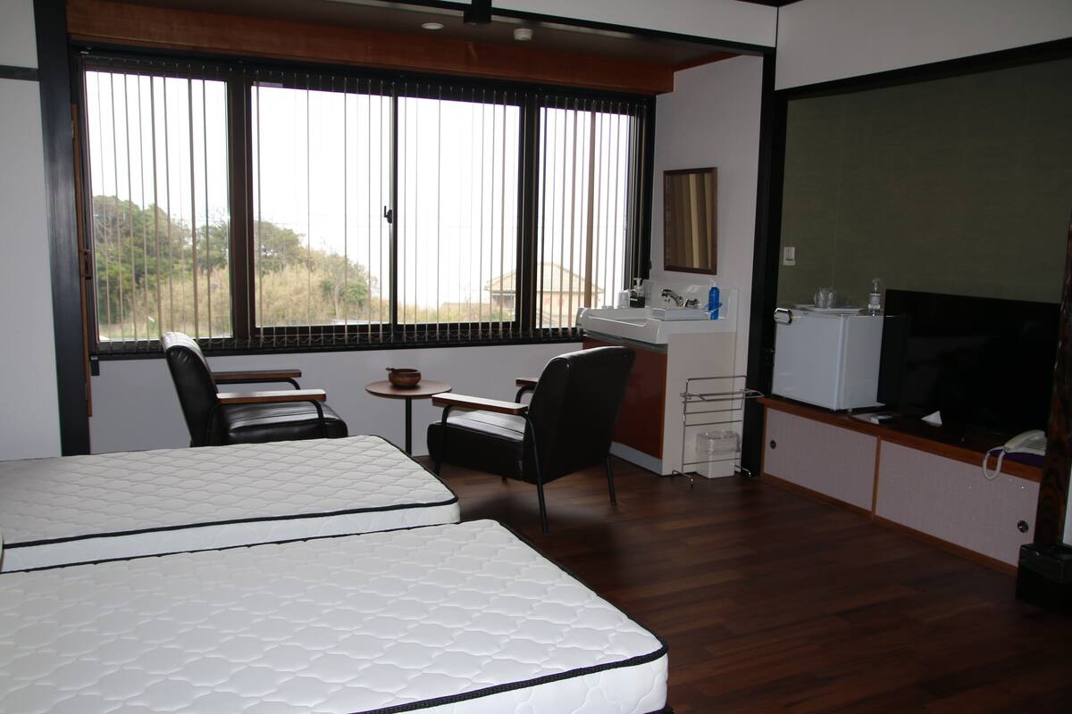 Una habitación con cama, escritorio, silla, televisor y ventana con persianas.