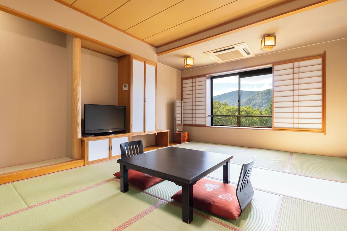 Une pièce de style japonais traditionnel, avec un sol recouvert de tatamis, une table basse, des chaises, un téléviseur, des portes coulissantes et une vue sur les montagnes.