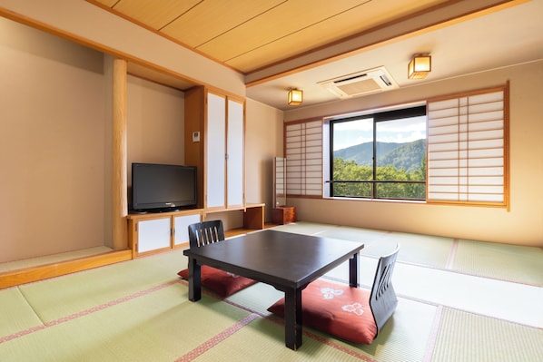 A traditional Japanese room with tatami flooring, a low table, chairs, a television, sliding doors, and a view of mountains.