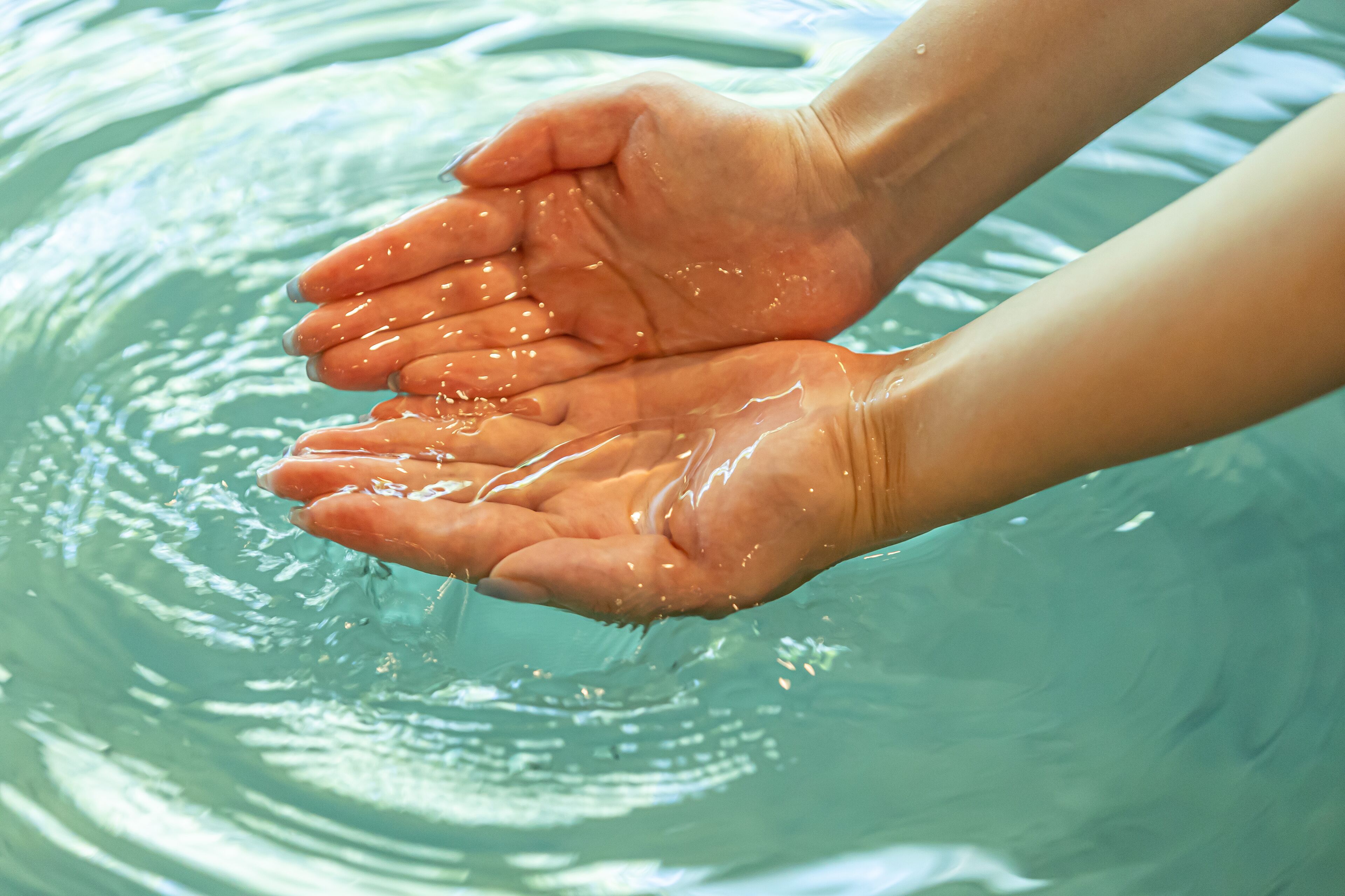 Manos llenas de agua, evocando un ambiente de piscina o spa.