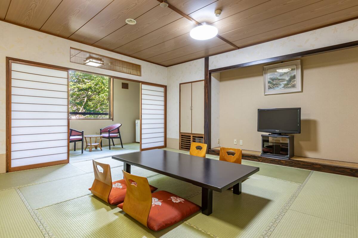 Une pièce de style japonais traditionnel, avec un sol recouvert de tatamis, une table basse et des portes coulissantes donnant sur un espace extérieur.