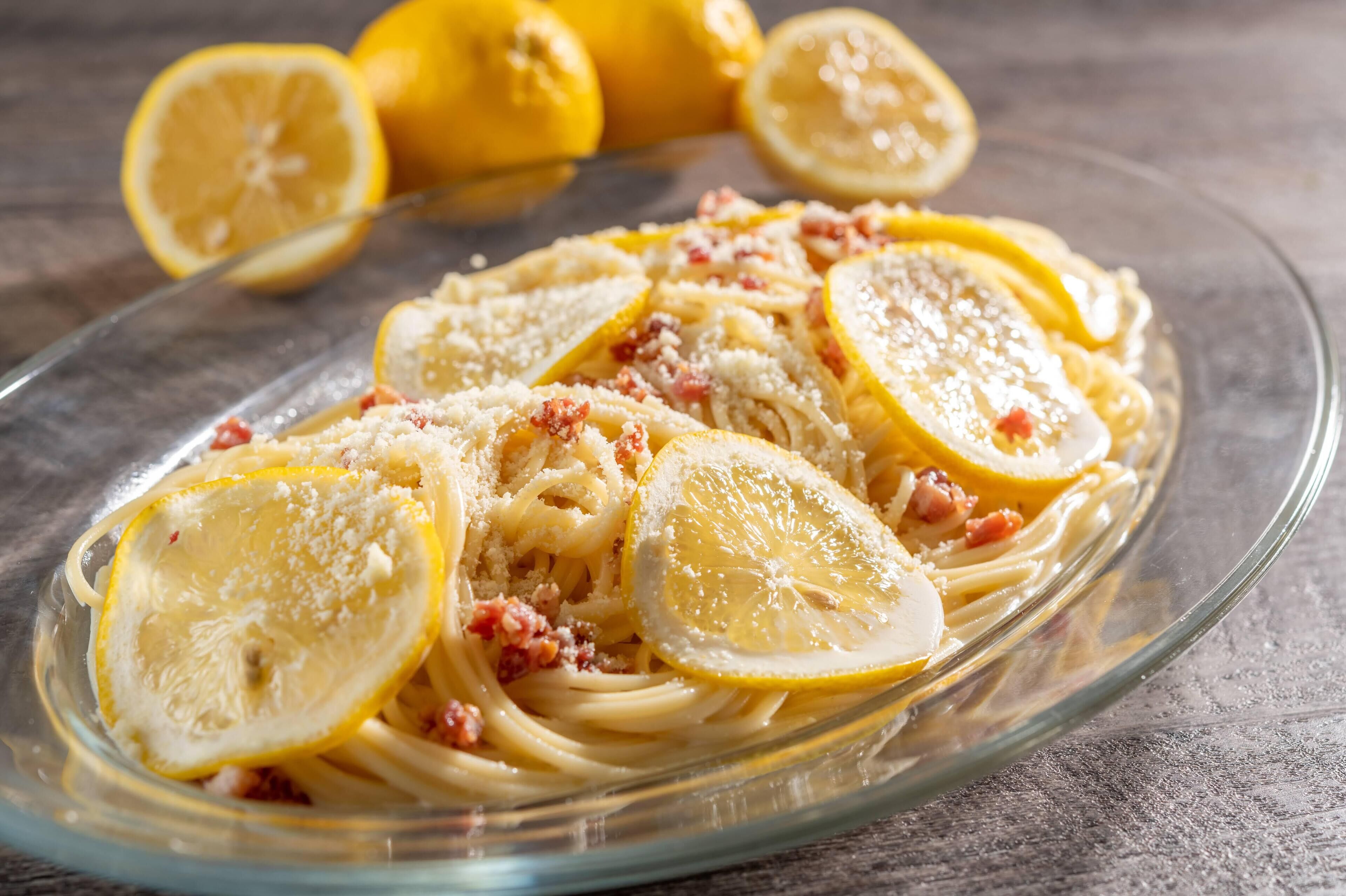 A plate of pasta with lemon slices and bacon bits.