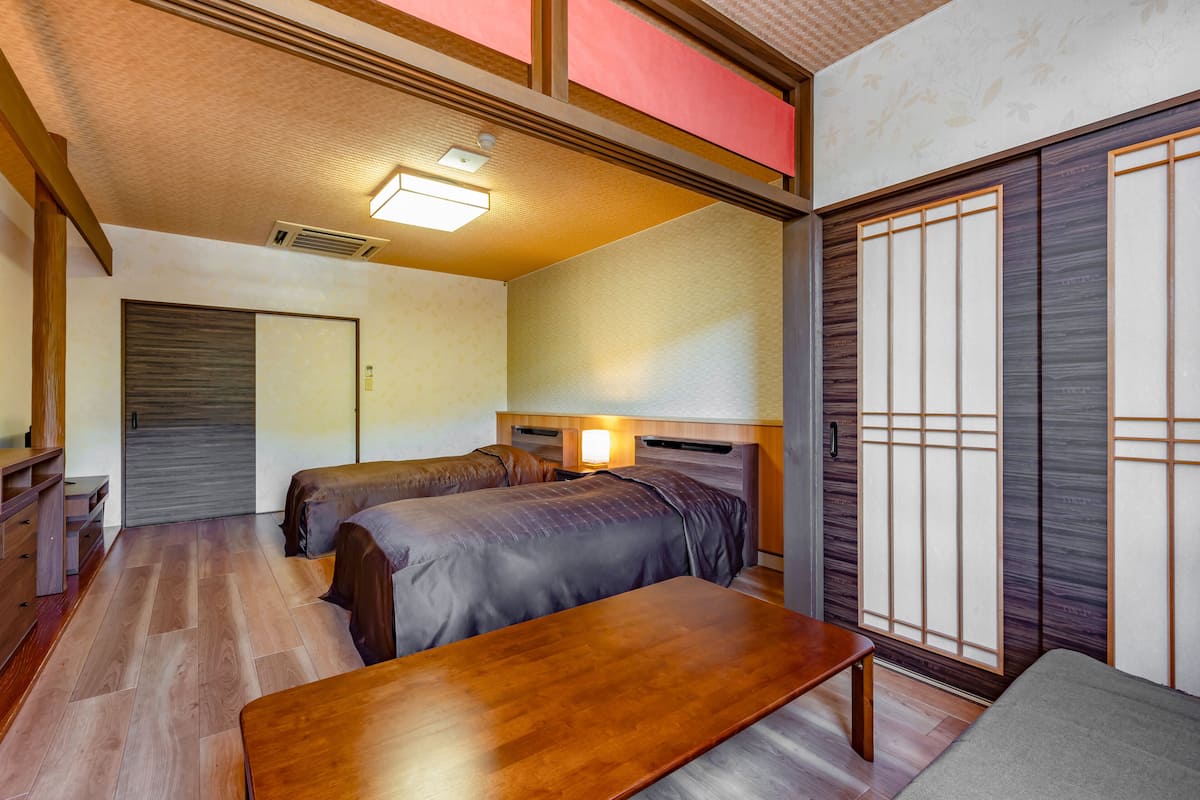 Une pièce de style japonais traditionnel, avec deux lits, une table en bois et des portes coulissantes.