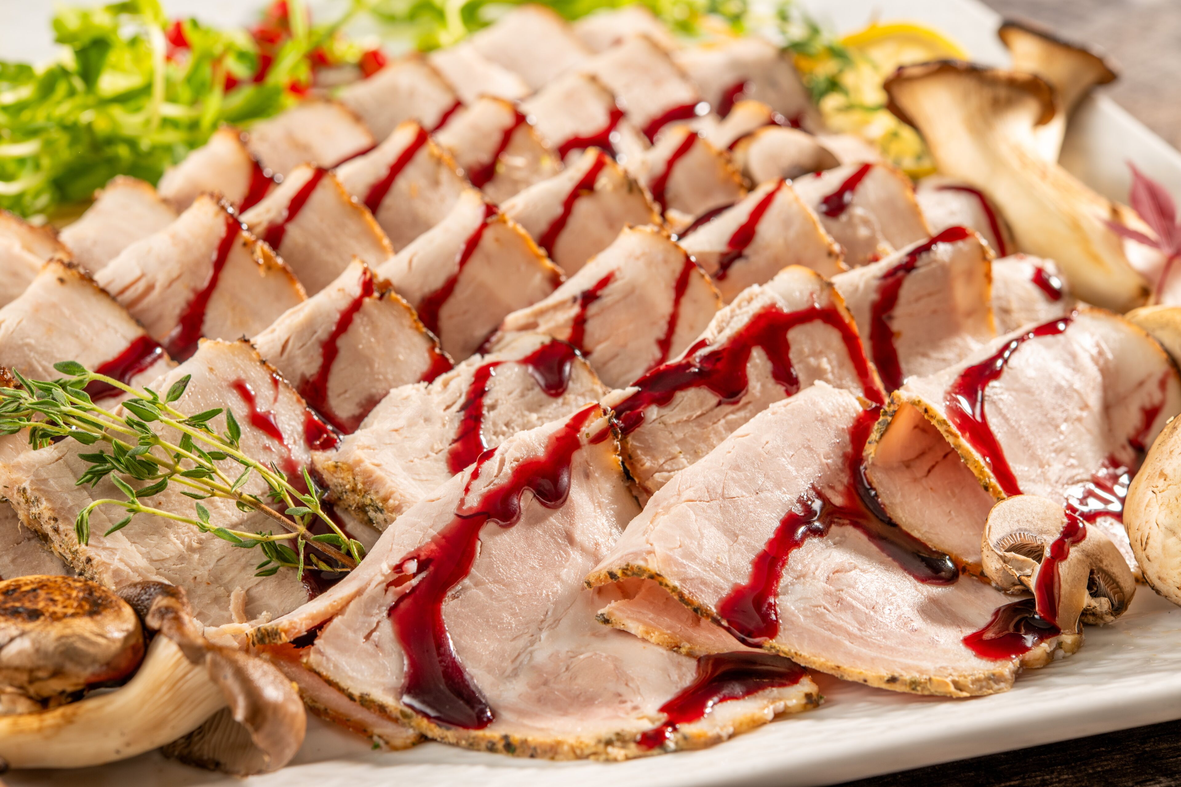 A plate of sliced meat with a red sauce, garnished with herbs and mushrooms.