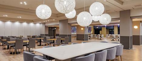 A spacious conference room with a long table and multiple chairs, surrounded by modern pendant lights.