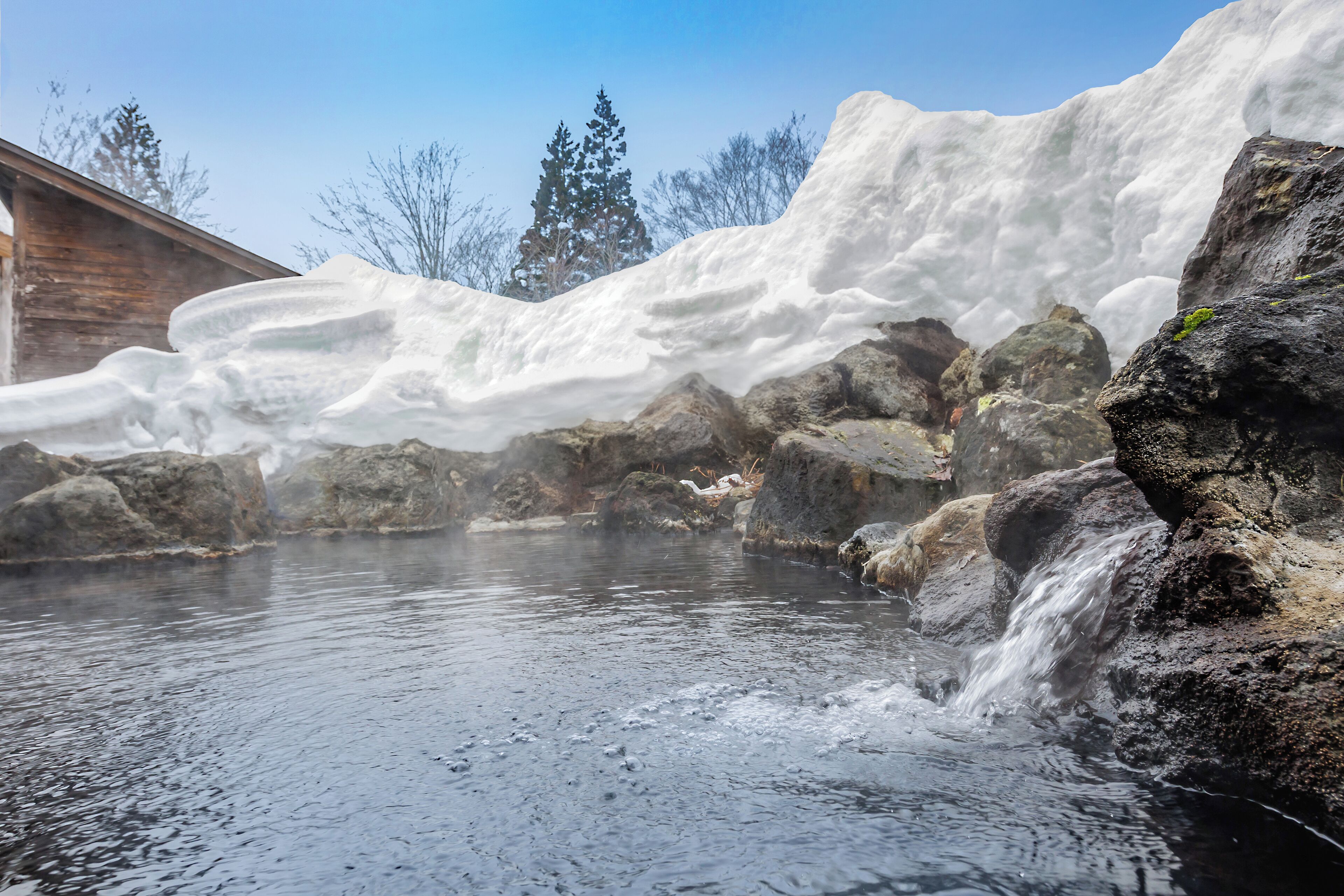 A natural hot spring with a wooden cabin in the background.