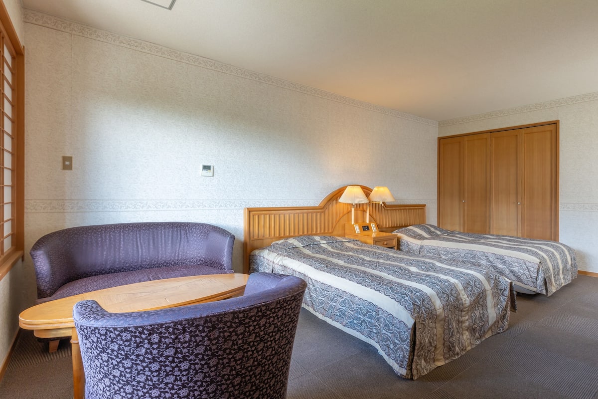 Une chambre d’hôtel avec deux lits, un canapé, une petite table et une armoire en bois.