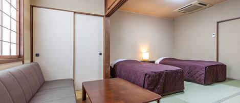 A traditional Japanese room with tatami flooring, a low wooden table, a cushioned bench, and two beds with purple bedding.