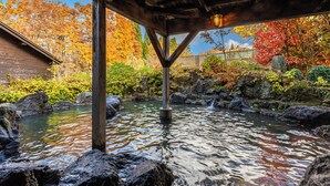 Una estructura de madera sobre un arroyo con rocas y follaje otoñal al fondo.