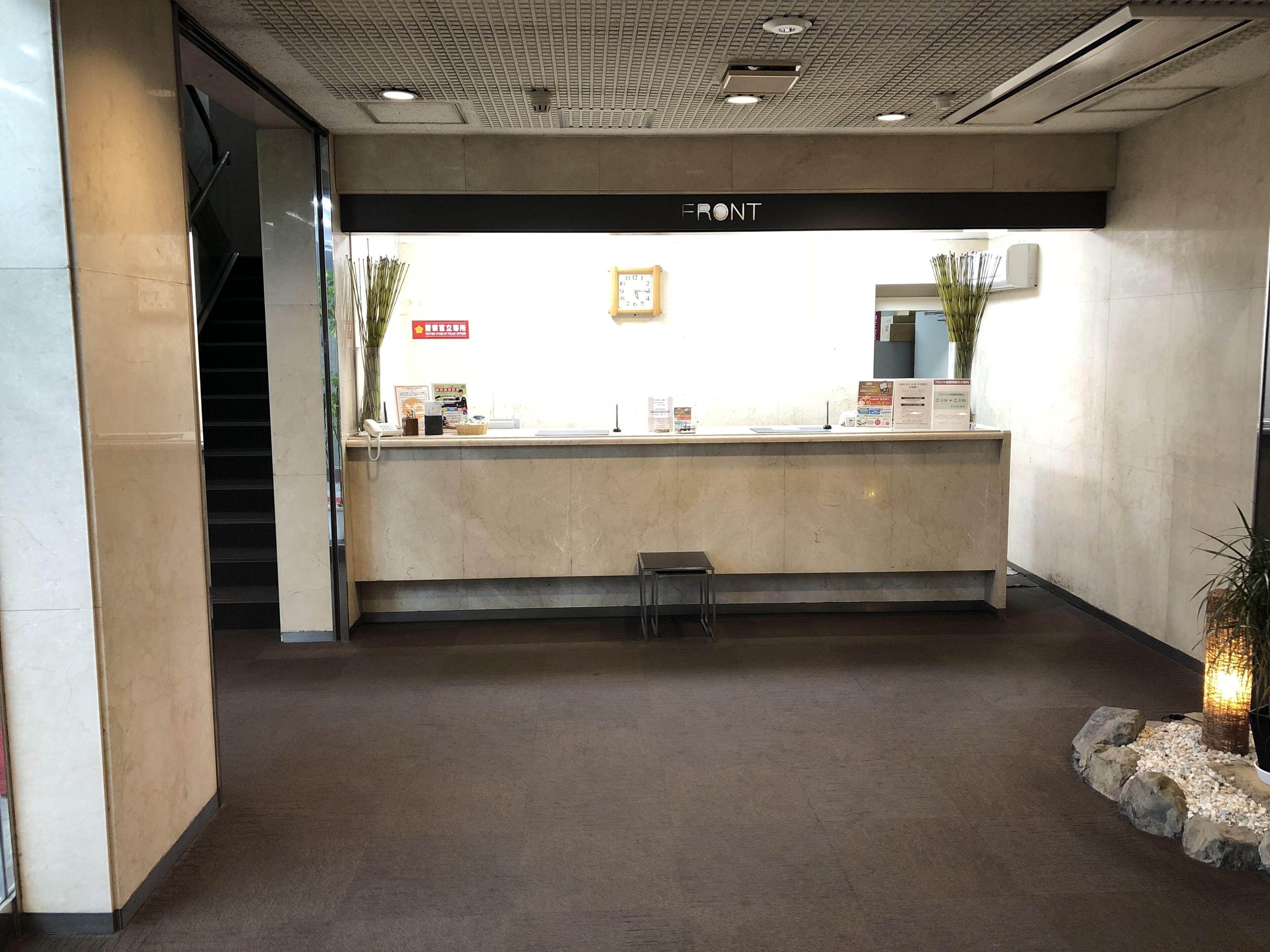 Un espace d’accueil doté d’un comptoir en marbre, d’une horloge et d’un escalier menant à un niveau supérieur.