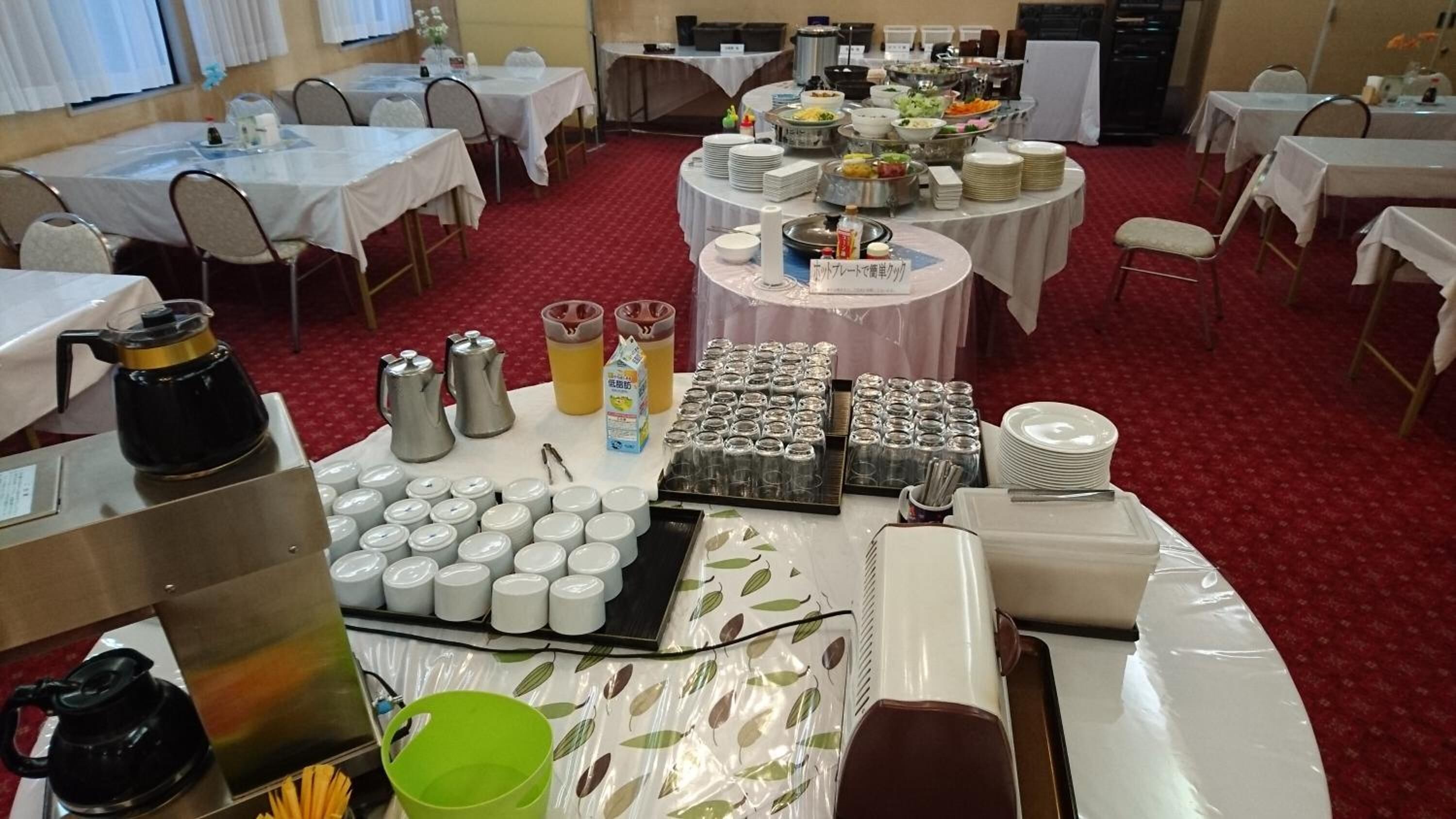 Un salón de banquetes con mesas redondas cubiertas con manteles blancos, equipado con platos, vasos y una variedad de recipientes para comida y bebidas.