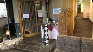 A reception area with a wooden door, a reception desk, and a waiting area with a sofa. - Hotel Hikari Hills (Hikari)