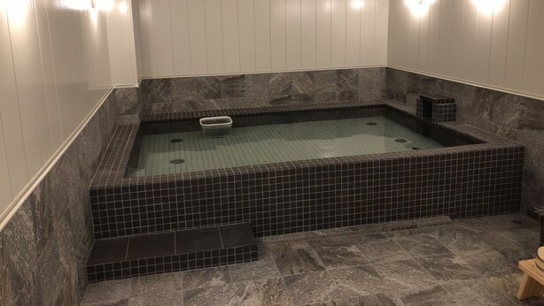 A spa room with a rectangular hot tub, tiled walls, and a marble floor. - Hotel Hikari Hills (Hikari)