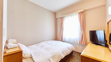 A hotel room with a bed, a desk with a telephone, a television, and a window with curtains.