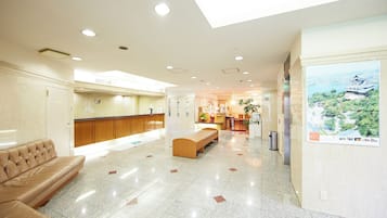 A hotel lobby with a reception desk, a seating area, and a poster on the wall.