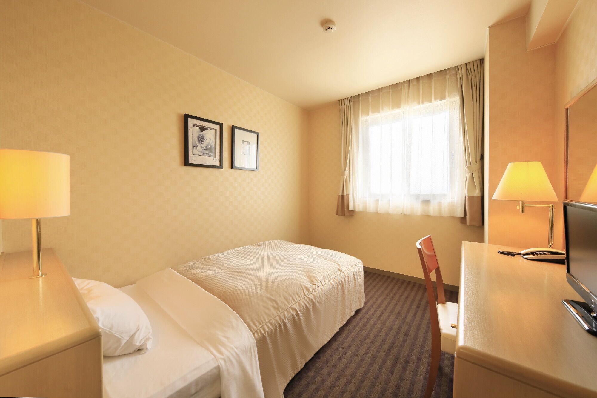 Een hotelkamer met twee bedden, een bureau met stoel, een televisie en twee ingelijste foto's aan de muur.