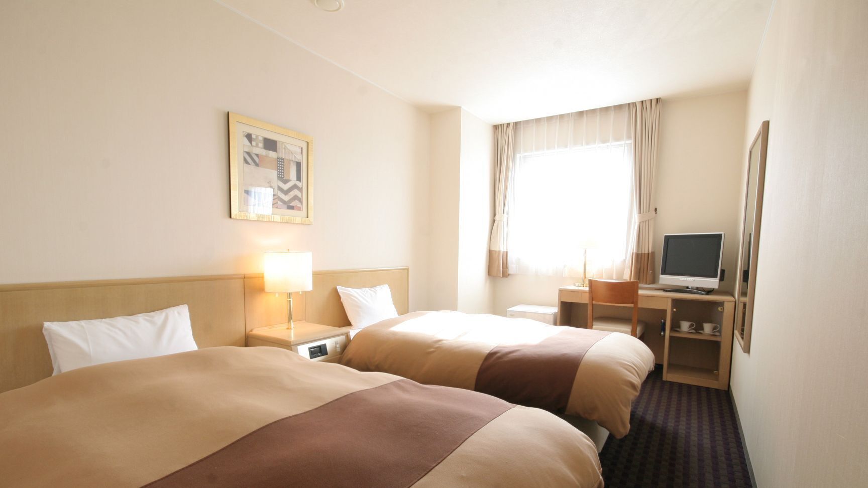 Habitación de hotel con dos camas, un escritorio con computadora, televisión y ventana con cortinas.