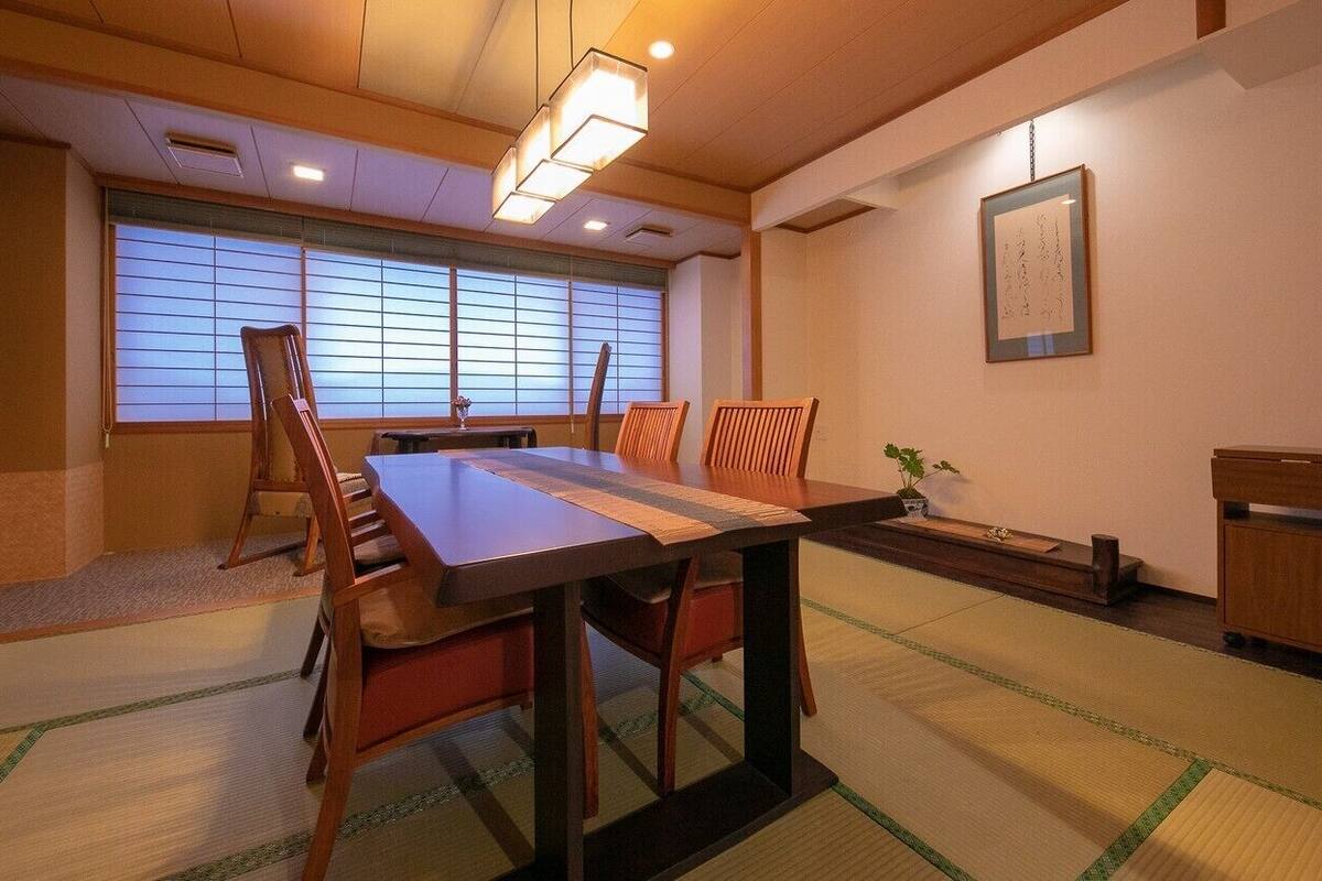 Ein traditioneller japanischer Raum mit Tatami-Böden, einem niedrigen Tisch, Holzstühlen, einem kleinen Schrank und einem Fenster mit Shoji-Bildschirmen.