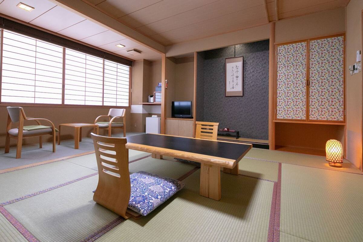 Ein Raum mit Tatami-Matten, einem Tatami-Tisch, Stühlen, einem Fernseher und einer traditionellen japanischen Laterne.