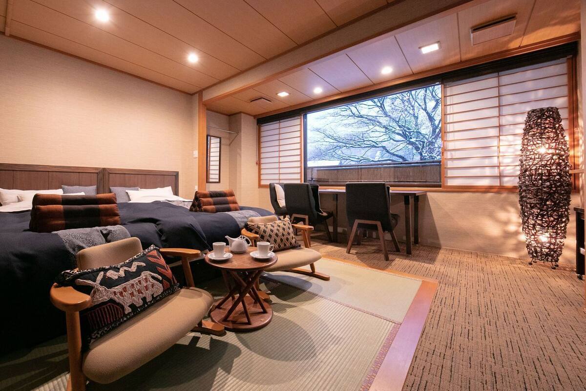 Ein Hotelzimmer mit zwei Betten, einer Sitzecke mit Sesseln und einem Tisch sowie einem großen Fenster mit Blick.
