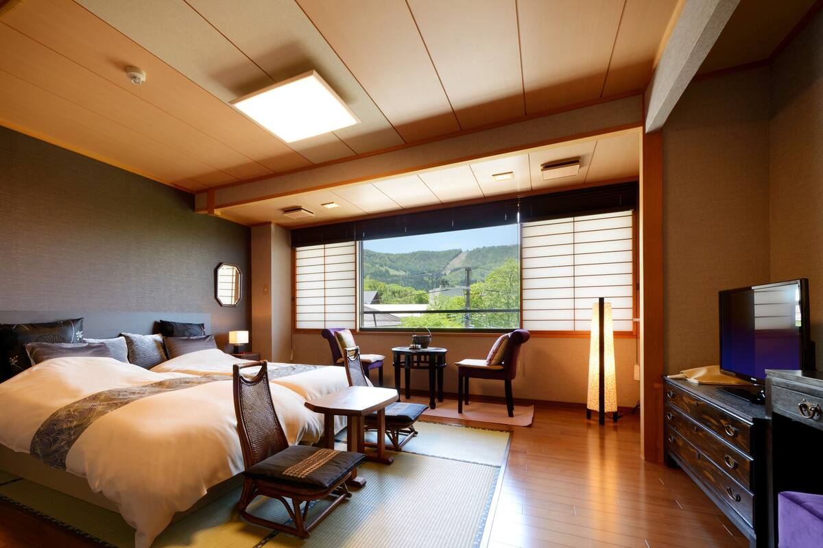 Ein Hotelzimmer mit Bett, zwei Sesseln, einem Schreibtisch, einem Fernseher und Blick auf einen Berg.