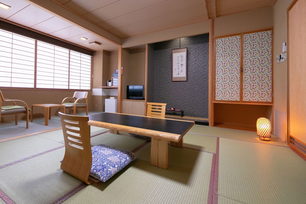A traditional Japanese room with tatami flooring, a low table, wooden chairs, a television, and a shoji screen.