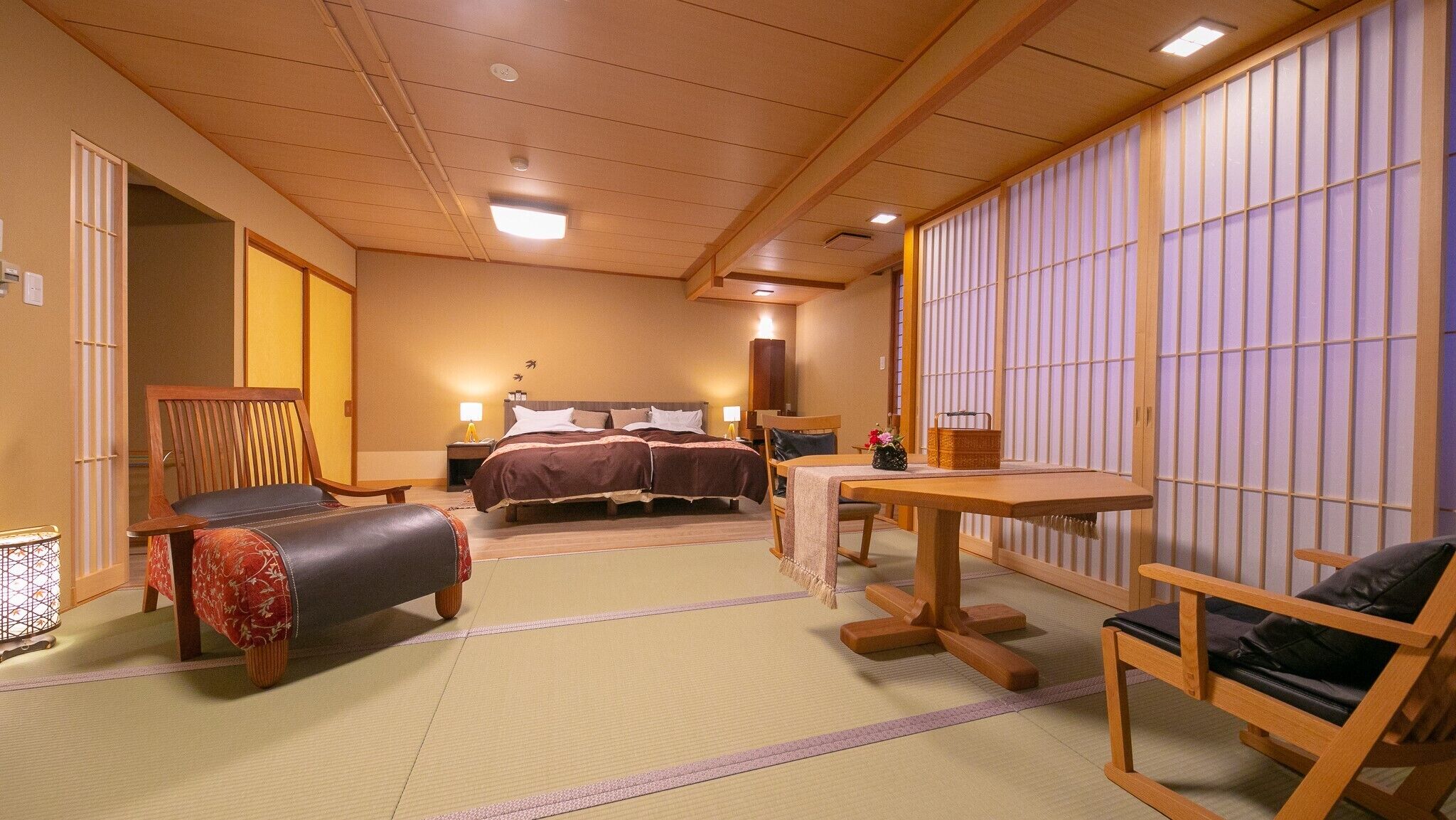 Perinteinen japanilaistyylinen hotellihuone, jossa on tatamimatto, sänky, työpöytä ja oleskelualue.