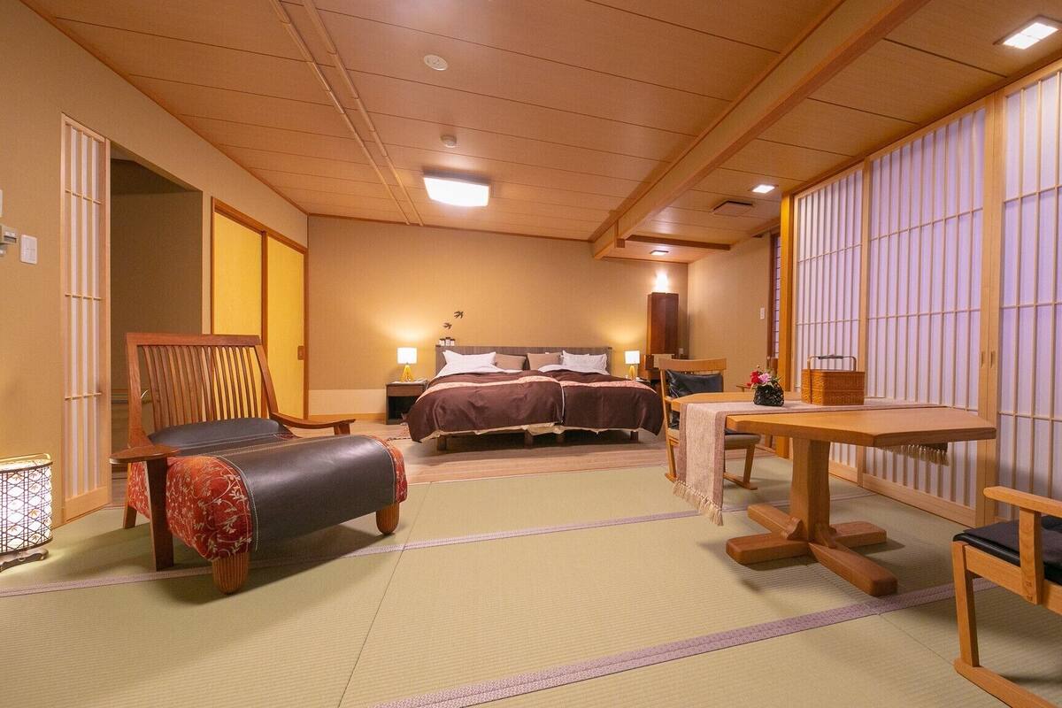 Ein traditionell gestaltetes Hotelzimmer im japanischen Stil mit Tatami-Böden, einem Bett, einem Schreibtisch und einer Sitzecke.