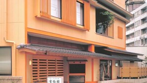 Un edificio de varios pisos con fachada tradicional, un letrero que indica un negocio o servicio, y una entrada protegida por una reja.
