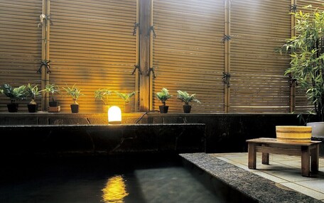 A tranquil indoor water feature with a bamboo backdrop, a small wooden table, and potted plants.
