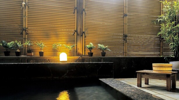 Una fuente interior tranquila con un fondo de bambú, una pequeña mesa de madera y plantas en macetas.