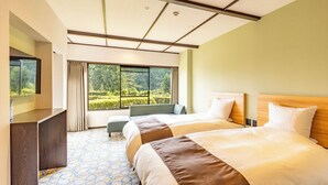 Een hotelkamer met twee bedden, een bureau, een raam met uitzicht op groen en een vloer met een patroon.